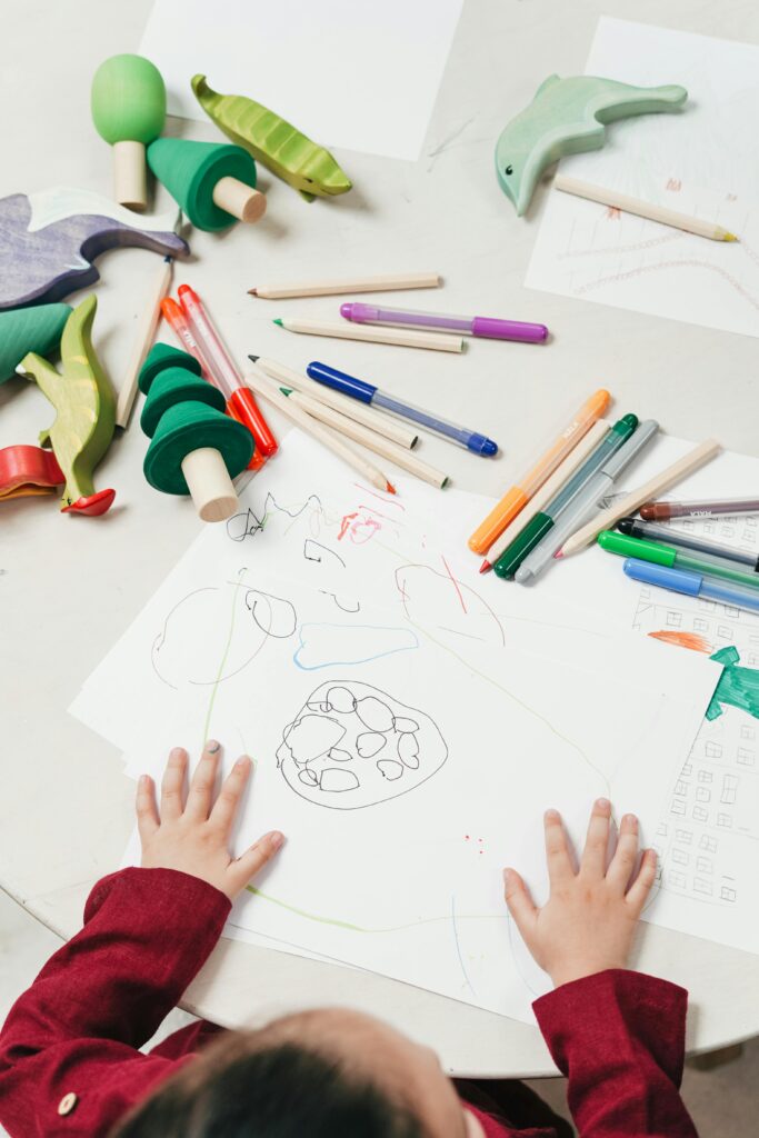 pexels-photo-3662630-3662630 A child engages in creative drawing with colored pencils surrounded by wooden toys on a table.